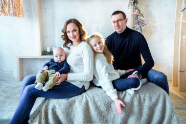 Mutlu anne ve baba, kız kardeş ve erkek kardeş büyük, parlak bir yatak odasında yatıyorlar. Noel dekoru ve ışıklar. Büyük mutlu bir aile. Ebeveyn sevgisi ve ebeveynlik kavramı