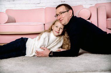 Baba sevgisi, kız babaya sarılıyor. Evdeki rahat, parlak bir odada pembe bir kanepenin yanında uzan. Siyah beyaz elbiseler. Ebeveyn sevgisi ve nesiller boyu muhalefet kavramı.