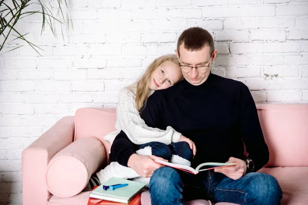 Amor paternal, hija abraza a papá. tumbarse en el suelo cerca de un sofá rosa en una acogedora habitación luminosa en casa. Ropa blanca y negra. El concepto de amor parental y la oposición de generaciones — Foto de Stock