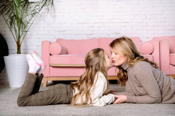 young woman and little daughter .The houses lie on the floor near the sofa, hugging and laughing, caring and tenderness. mother's love. Kiss, tenderness and care of mom.The concept parenting