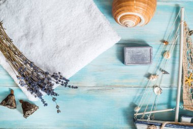 Kaplıca, beyaz havlu, mavi ahşap arka plan. Lavanta ve kuru nilüfer çiçeği. Deniz kabuğu. Mor banyo sabunu. Kabuklu ahşap tekne. Tatil konsepti düzdü. Üst Manzara. Boşluğu kopyala.