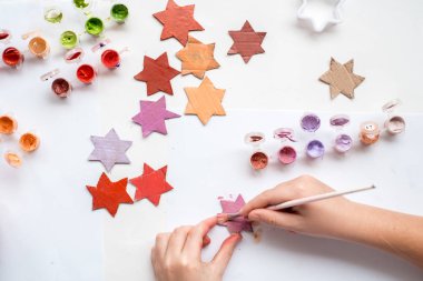 Bir çocuk kartondan bir yıldız oyuyor. Noel süsü, Noel çelengi, el yapımı ve sıfır atık. Beyaz arka planda bir çocuğun elleri. Div