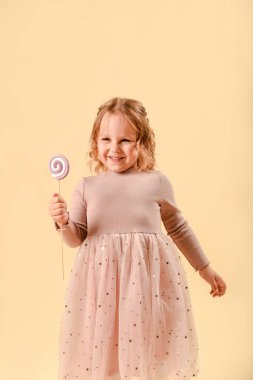 Şekerli küçük bebek. Pembe zarif bir elbise. Tatil ya da doğum günü. Elinde tatlılar var. Stüdyoda hafif bir arka planda.