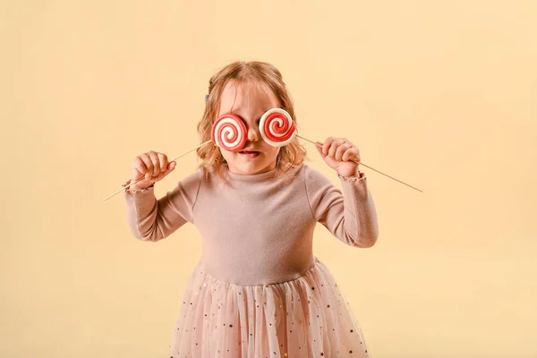Ett litet barn med godis. Rosa elegant klänning. Semester eller födelsedag. Sötsaker i handen. på en ljus bakgrund i studion. — Stockfoto