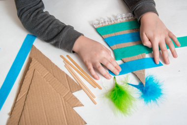 Yaratıcı X mas diy dekoru. Çocuklarla el işi. Bir çocuğun elleri. Kartondan mavi ladin, keçe ve boncuklar. Kutuların ve kumaş parçalarının kalıntıları. Sıfır İsraf Noel kavramı.