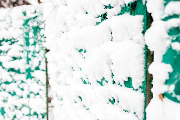 Snow-covered blue old rural wooden fence. Winter in the village. Snow and icicles are everywhere. New Year and Christmas mood. Severe frost. Ice in the puddles. Slippery roads.