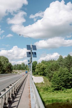 Güneş enerjisi paneli. Bulutlu mavi gökyüzü, geniş otoban ve orman. Yenilenebilir güneş enerjisi kavramı..