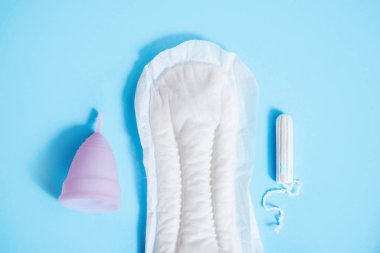 Mavi arka plan üzerine kurulmuş kadınsı mahrem hijyen. Hijyenik ped, pamuklu çubuk veya bardak. Modern bir kadının seçimi.