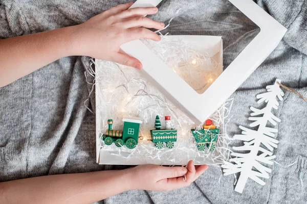 Mãos de uma criança segurando um presente, Um brinquedo de trem de madeira está carregando presentes de Ano Novo. Em uma camisola cinza de malha aconchegante. vista superior — Fotografia de Stock