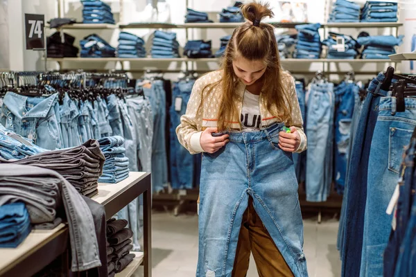 Frau wählt Jeans im Bekleidungsgeschäft. Teenie-Mädchen kauft Jeans im Einkaufszentrum. — Stockfoto