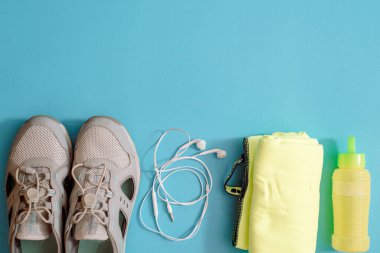 Spor malzemelerinin düz karesi. Spor, koşu ayakkabıları, kulaklıklar, bir bardak temiz su ve mavi arka planda mikrofiber havlu. Boşluğu kopyala