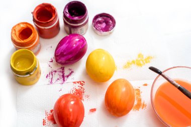 Paskalya yumurtasını fırçayla boyayan insan eli. Sarı, turuncu, kırmızı ve mor yumurta. Paskalya için yumurta boyuyorum.