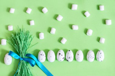 Paskalya arkaplanı yumurta ve bir buket yeşil çimen. Beyaz yumurta deseni. Bayram düzlüğü kompozisyonu, komik Paskalya konsepti. Mavi kurdele, yeşil arka plan..