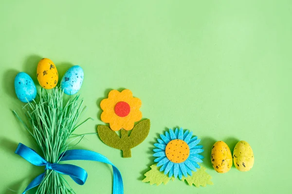 Пасхальный фон с яйцами и букетом зеленой травы и цветными пасхальными яйцами. Праздничная плоская композиция, забавная пасхальная концепция, голубая лента, зеленый фон — стоковое фото