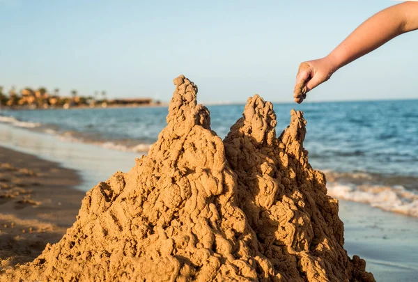 Sand castle made of sand by the hands of a child on the shore.Sea at sunset, white sand on the beach.Sunset sun, yellow light.