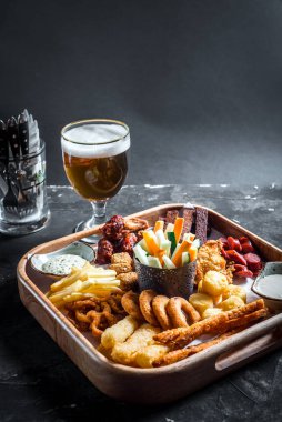 Sosisler, tavuk kanatları, kızarmış ekmekler, soğan halkaları ve ahşap tahtada ahşap halkalar sos ve bir bardak birayla oktoberfest 'e. Boşluğu kopyala