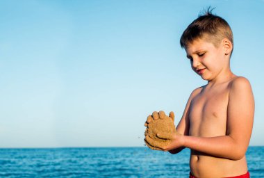 Deniz tatili. Kumsaldaki sevimli çocuk kumla oynuyor. Kumdan kale ve pasta kalıpları. Gün batımı, mavi gökyüzü ve rahat seyahat konsepti. Boşluğu kopyala.