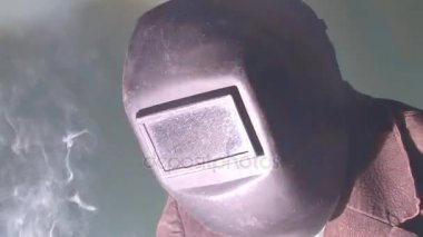 Kapalı kaynak maskesinde çalışan bir kaynakçı elektrotlar, yanıp sönen ışıklar ve sıcak metalle kaynak yapar..