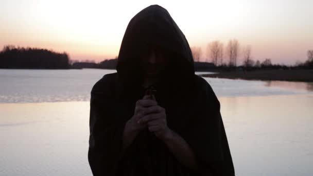 一个和尚在湖岸边祈祷 拿着十字架 — 图库视频影像