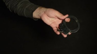 Bir adam siyah arka plana metal kelepçe takıyor, tutukluyor ve gözaltına alıyor..