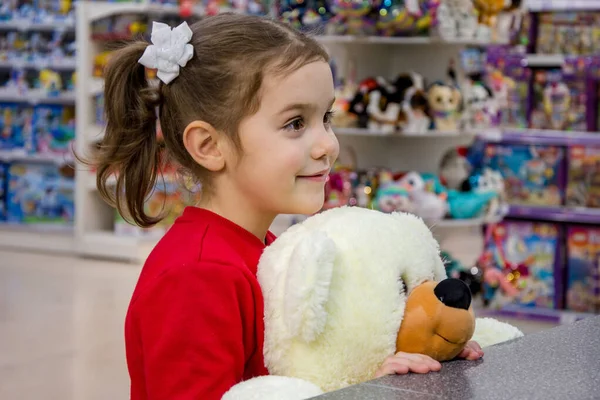 女孩笑着 手里拿着一只大北极熊 站在商店里的儿童玩具中间 儿童的情感 等待礼物和购买 — 图库照片