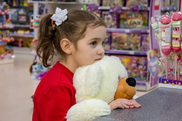 女孩很伤心 手里拿着一只大北极熊 站在商店里的儿童玩具中间 儿童的情感 等待礼物和购买 — 图库照片