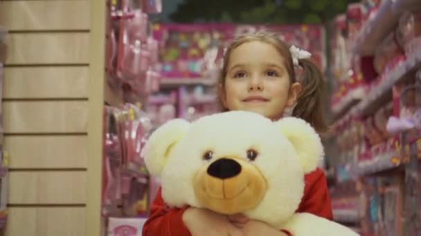 女の子は手に大きなホッキョクグマを持ち 子供のおもちゃの間で店に行きます 子供の感情や贈り物への期待 — ストック動画