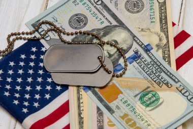 Amerikan bayrağının ve dolarların arka planında ordu kimlik madalyonları yatıyor. Konsept: Ordu emekliliği, orduda maaş, ordu sigortası, paralı askerler ve müteahhitler.
