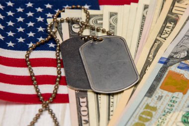 Amerikan bayrağının ve dolarların arka planında ordu kimlik madalyonları yatıyor. Konsept: Ordu emekliliği, orduda maaş, ordu sigortası, paralı askerler ve müteahhitler.