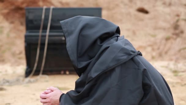 一位身穿黑袍 头戴头巾的僧人坐在空地上 在炉边取暖 — 图库视频影像