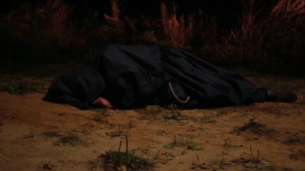 一个身穿黑色长袍的僧人躺在地上的黑暗中 一个火圈在他周围燃着 — 图库视频影像