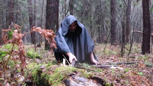 黒い衣を着た僧が森の中の火のために木をレイアウトします — ストック動画