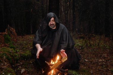 Siyah cüppeli bir keşiş ormanda ateşin yanında oturur ve kehanet topuna bakar. Mistisizm ve büyü, büyücüler ve cadılar 6