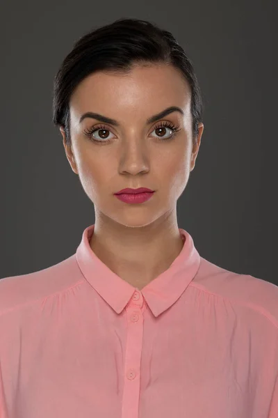 一位30 35岁的年轻女子穿着一件灰色背景的粉色衬衫 抑制了她的情绪 也许她在办公室工作 销售人员 — 图库照片