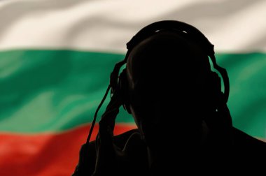 Bulgaristan bayrağının arka planında kulaklıklı bir adamın silueti, bir konuşmayı gizlice dinlemek, gizli ajan, askeri müdahale, darbe, casus ve istihbarat, aydınlatma.