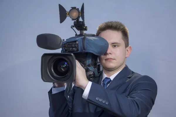 Portrait of a young man in a suit, who stands holding a TV camera on his shoulder on a light background.  The operator works with a video camera, shoots a report or conducts Studio shooting