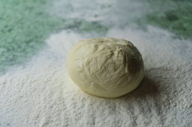 Bir dilim pizza hamuru mutfak masasının üzerinde, fırında pişirmek için bir parça un.