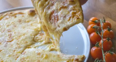 Domateslerin yanındaki beyaz tabakta duran peynirli pizzayı kırar.