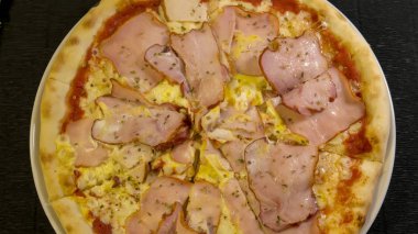 Peynirli, soslu, jambonlu, pastırmalı, füme tavuklu ve yumurtalı Karnos pizzası masada.