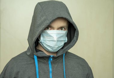 Kapüşonlu sweatshirt giyen, tıbbi maskeli genç bir adam beton bir duvara karşı. Avrupa 'daki gençlerin kişisel güvenliği.