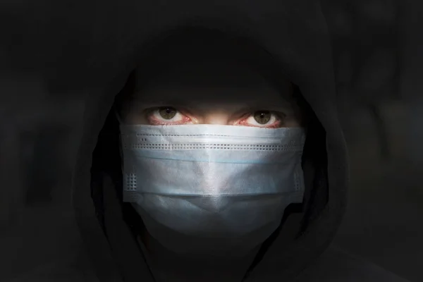 在黑暗的背景下 一个身穿蒙面运动衫 戴着医疗面罩的年轻人 欧洲年轻人的人身安全 — 图库照片