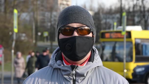 一个男人站在人行横道上 戴着黑色的医疗面罩和防护太阳镜 人们走过 照顾好你的健康 在城市预防疾病 — 图库视频影像