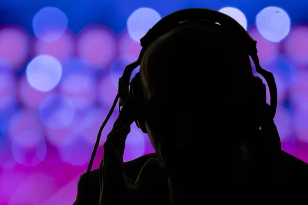 Egy Fejhallgatós Férfi Sötét Sziluettje Város Sokszínű Csillogásának Fényeinek Hátterében — Stock Fotó