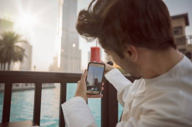 Arab young man taking photo on smartphone wearing Kandura in Dubai clipart