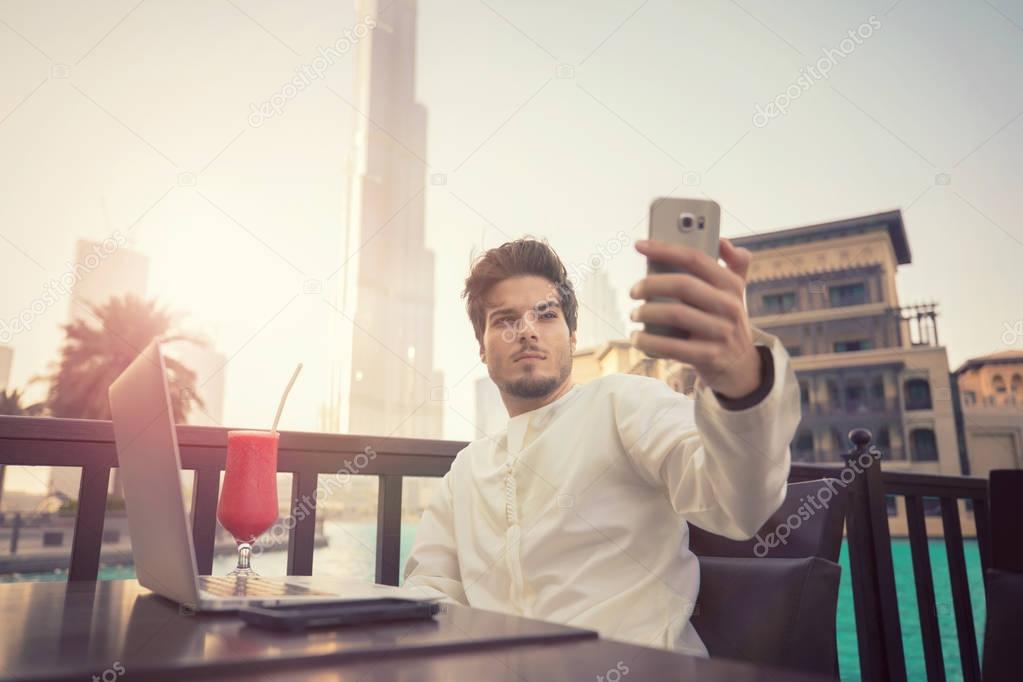 Arab young man taking selfie photo on smartphone wearing Kandura