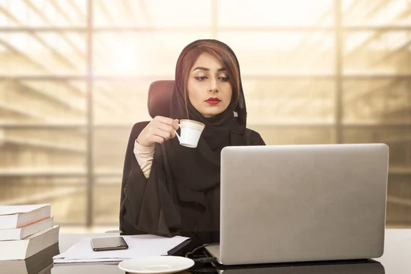 Bir ofis, çalışma masasında oturan Arap genç iş kadını
