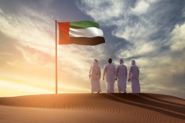 Emirati 'nin genç adamları çölde kum tepeciğinde durup Uae bayrağına bakıyorlar ve Uae bayrağını kutluyorlar.