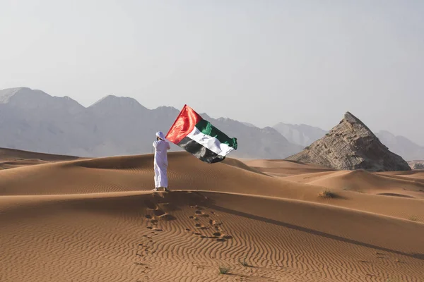 Uae bayrağını çölde tutan Arap adam Uae bayrağını ve Uae bayrağını kutluyor..