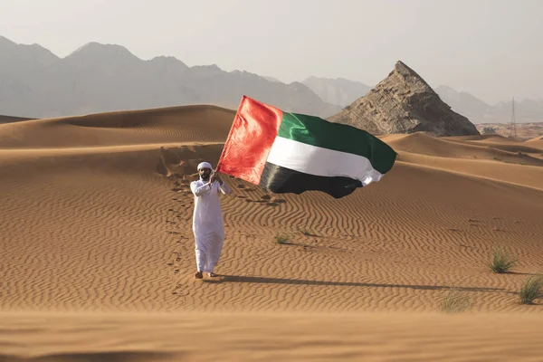 Uae bayrağını çölde tutan Arap adam Uae bayrağını ve Uae bayrağını kutluyor..