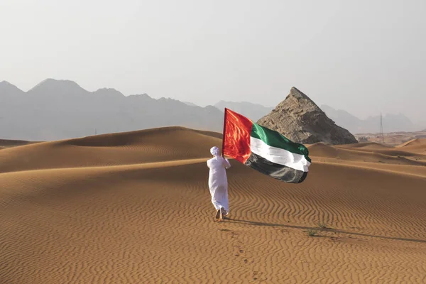 Uae bayrağını çölde tutan Arap adam Uae bayrağını ve Uae bayrağını kutluyor..